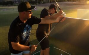 James Jordan guiding a student through a golf swing at the driving range at sunset.