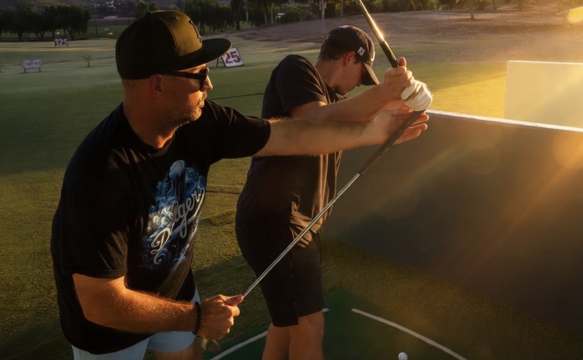 James Jordan guiding a student through a golf swing at the driving range at sunset.